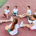 Coach or PE teacher sitting in a circle with with a group of young children on an outdoor athletics track