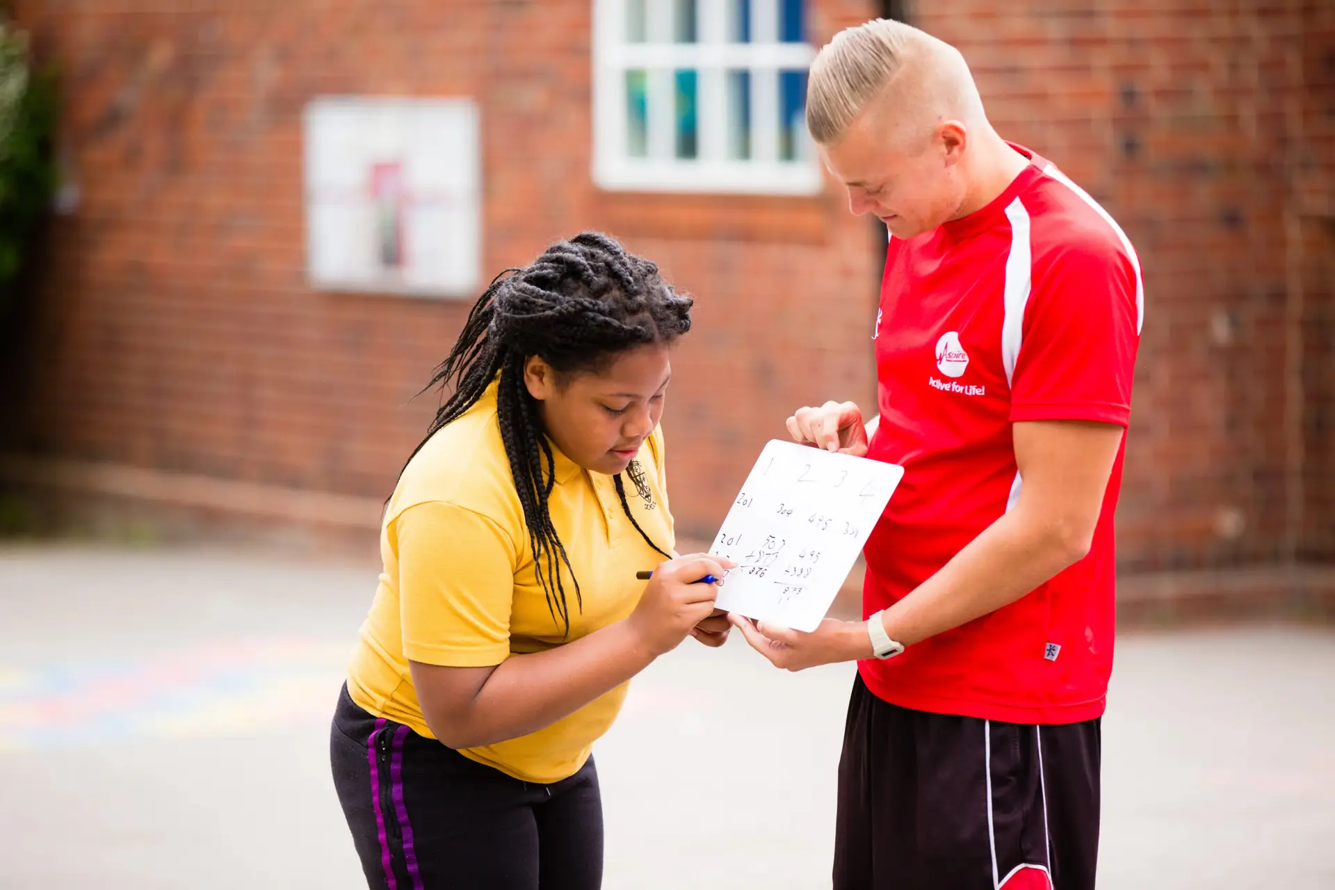 Young female student in sports clothing doing maths sums on a portable white board outdoors