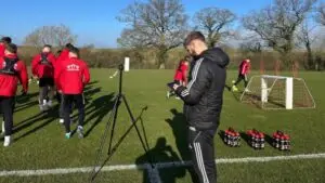 Oxford Brookes University student Keiran on a work placement monitoring data by the side of a football pitch as the team trains