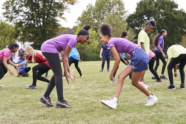 Two teenage girls in sportswear play an outdoor game. They are smiling at each other.