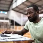 Man sat using laptop in sports hall