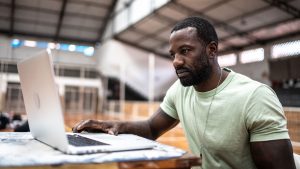 Man sat using laptop in sports hall