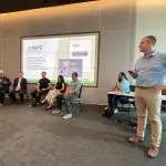 Spencer Moore stands beside a seated group of experts, leading a presentation