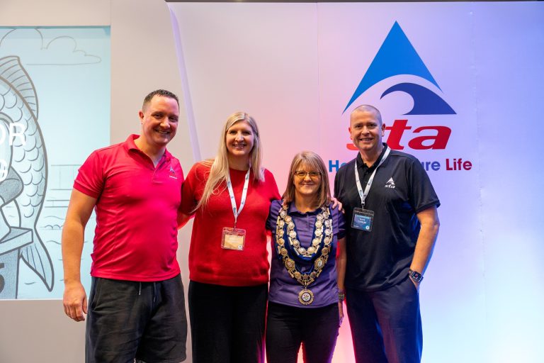 Ali is accompanied by Rebecca Adlington and two members of the STA. They all smile to the camera.