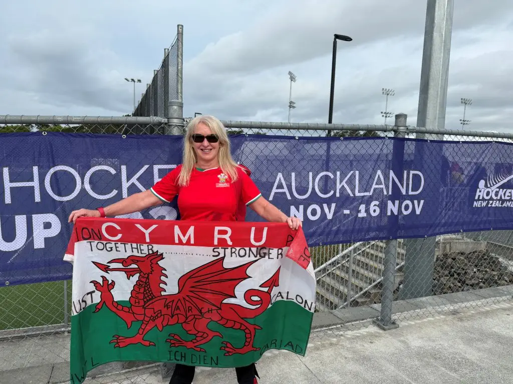 Stephanie holds a Welsh flag in front of a sign that says Auckland.
