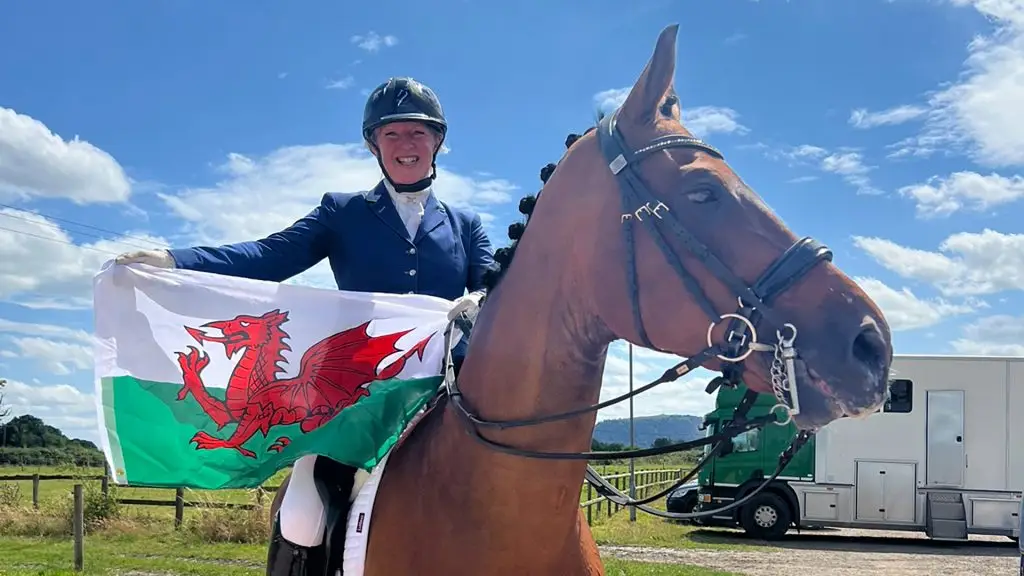 Stephanie is sitting on a horse holding a Welsh flag