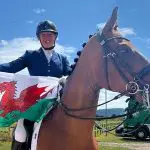 Stephanie is sitting on a horse holding a Welsh flag