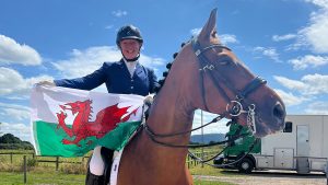 Stephanie is sitting on a horse holding a Welsh flag