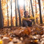 Woman sitting in forest looking up at trees