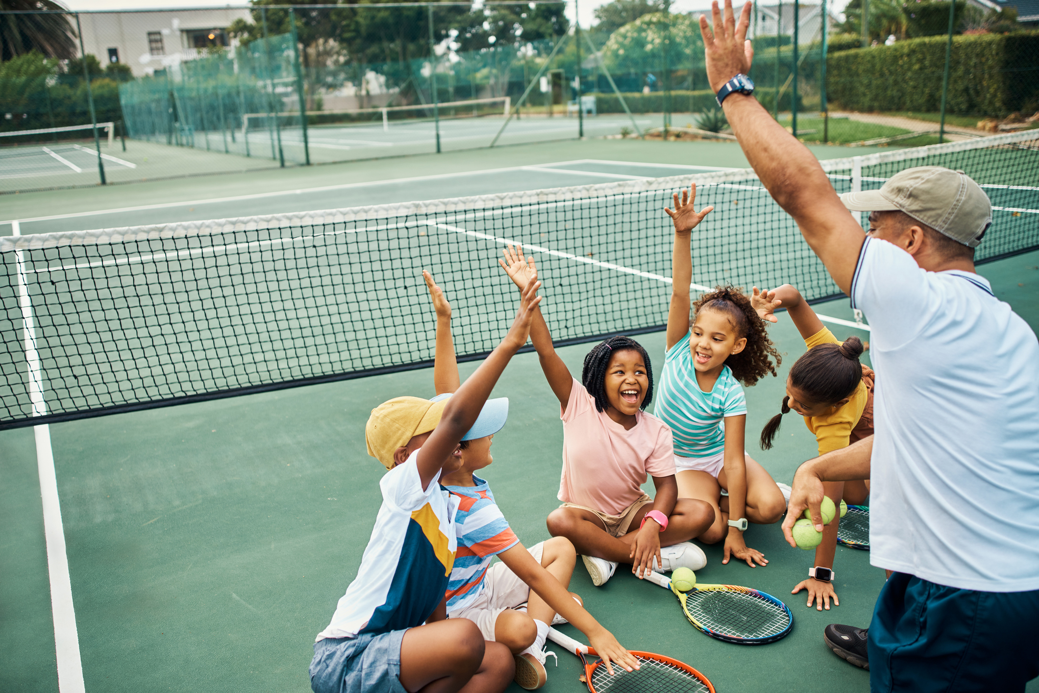 Children sit on the floor around a coach. They all have one hand in the air and are smiling