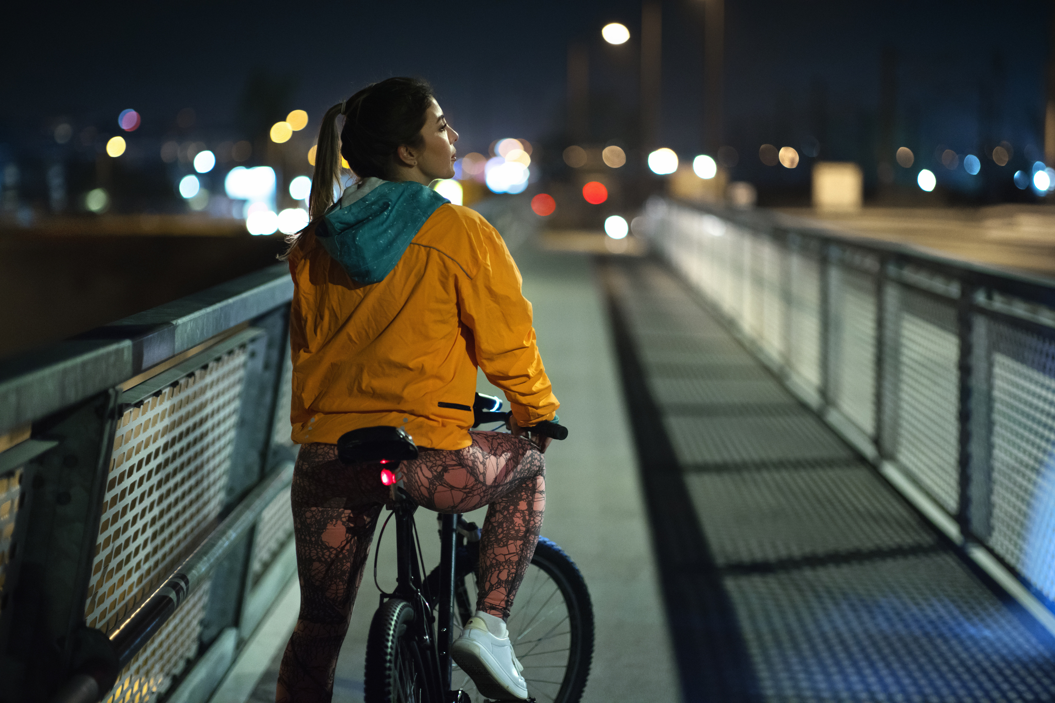 Rear view night shot of a young woman biking in the city street.