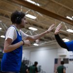 A young man wearing noise-cancelling headphones high fives his female basketball coach