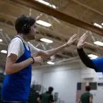 A young man wearing noise-cancelling headphones high fives his female basketball coach