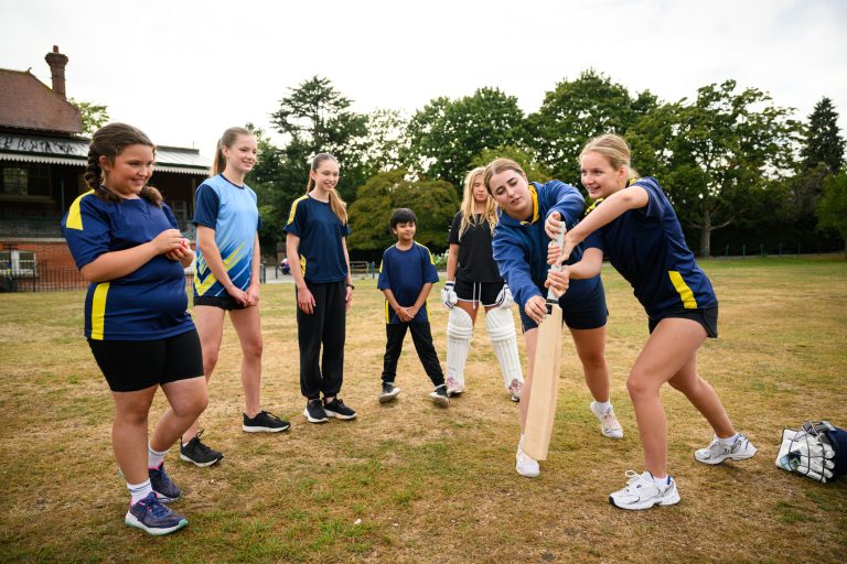 A young female coach is teaching a group of children how to hold a cricket bat