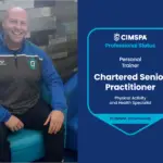 Liam sitting in a chair smiling at the camera. To the right is his professional status credential.