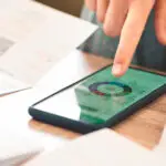 A hand hovers over a smartphone on a desk displaying a pie chart.