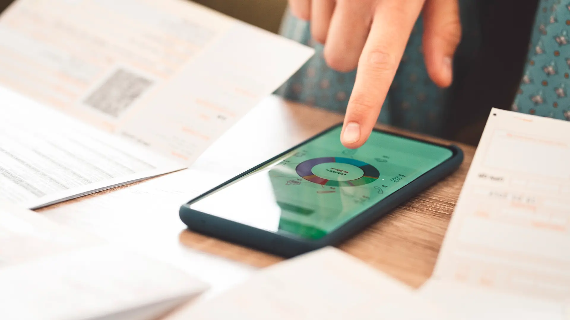 A hand hovers over a smartphone on a desk displaying a pie chart.