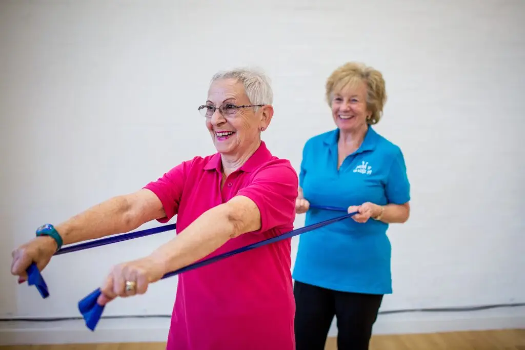 A trainer supports an older woman using resistance bands