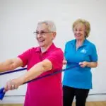 A trainer supports an older woman using resistance bands