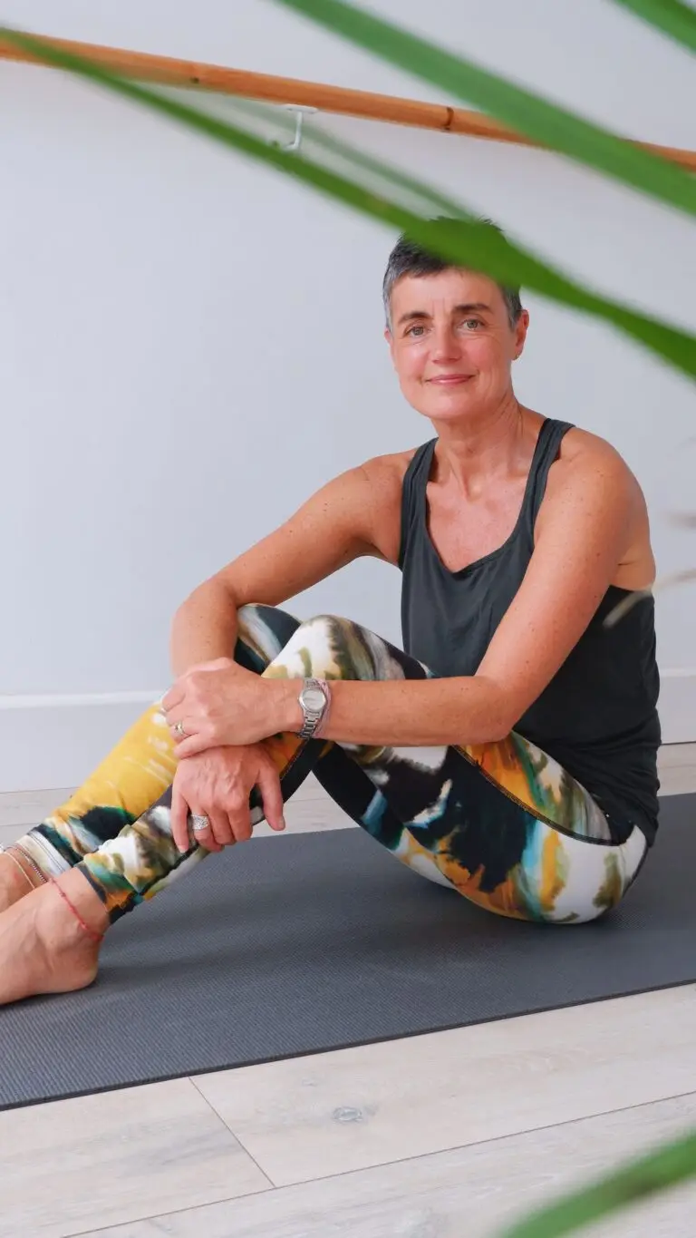 Sally Villain sits on a yoga mat facing the camera