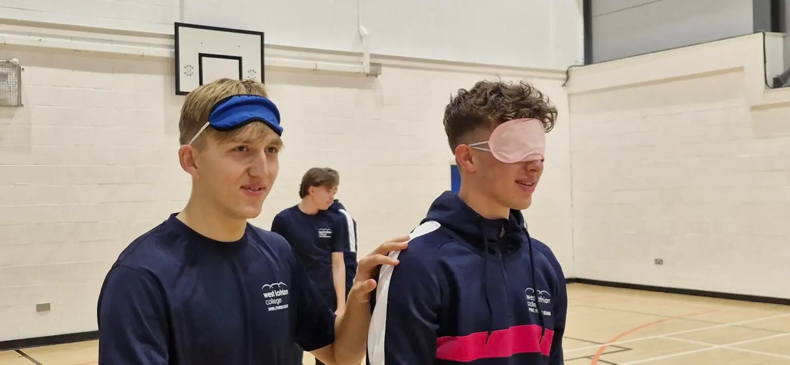 A blindfolded student is lead by another student who can see.