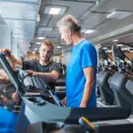A personal trainer guides a client using a treadmill, pointing at the screen