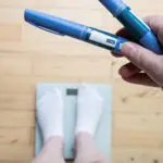 A person standing on scales holds weight-loss drug pens