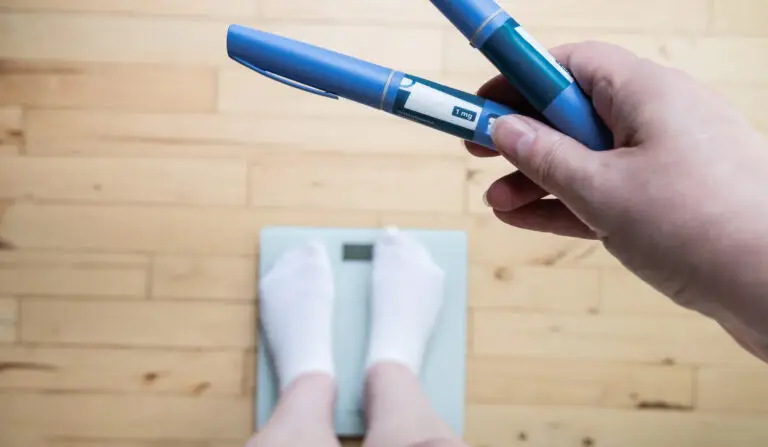 A person standing on scales holds weight-loss drug pens