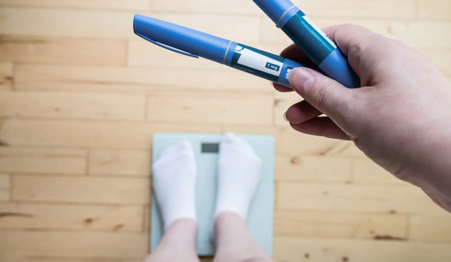 A person standing on scales holds weight-loss drug pens