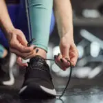 An unseen women ties the lace of her trainer
