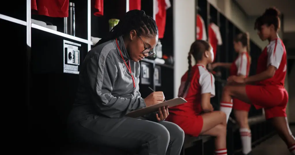 A female coach sits in a changing room and looks at a clipboard