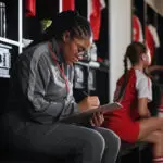 A female coach sits in a changing room and looks at a clipboard