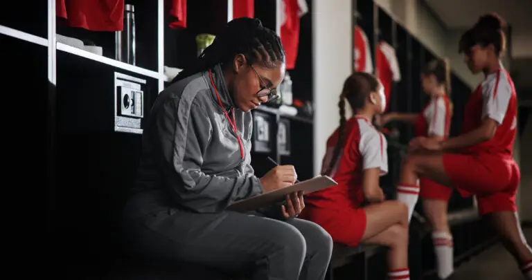 A female coach sits in a changing room and looks at a clipboard