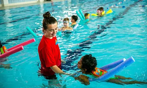 A swimming teacher in a pool with a class of children