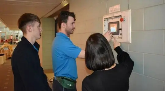 Three people look at a leisure centre control panel. Two are touching it.