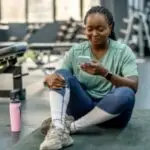 A woman sits on the floor of a gym looking at her phone