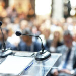 Microphones in focus at business conference, corporate presentation, workshop, coaching training, news conference, company meeting, public or political event. Public speaking concept.