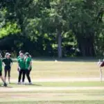 A women's cricket team stand on pitch in the sun