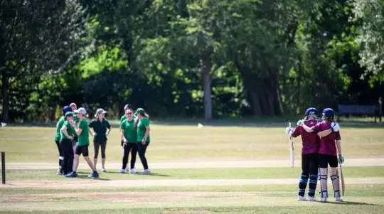 A women's cricket team stand on pitch in the sun