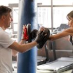A woman hits boxing pads held by a man