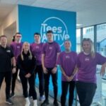 A group of young adults stand in front of a Tees Active logo in a leisure centre
