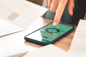 A hand hovers over a smartphone on a desk displaying a pie chart.