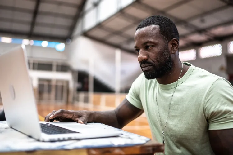 Man sat using laptop in sports hall