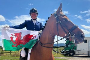 Stephanie is sitting on a horse holding a Welsh flag
