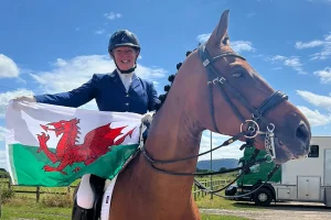 Stephanie is sitting on a horse holding a Welsh flag