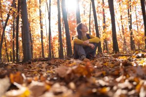 Woman sitting in forest looking up at trees