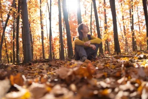Woman sitting in forest looking up at trees