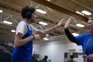 A young man wearing noise-cancelling headphones high fives his female basketball coach