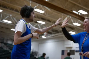 A young man wearing noise-cancelling headphones high fives his female basketball coach